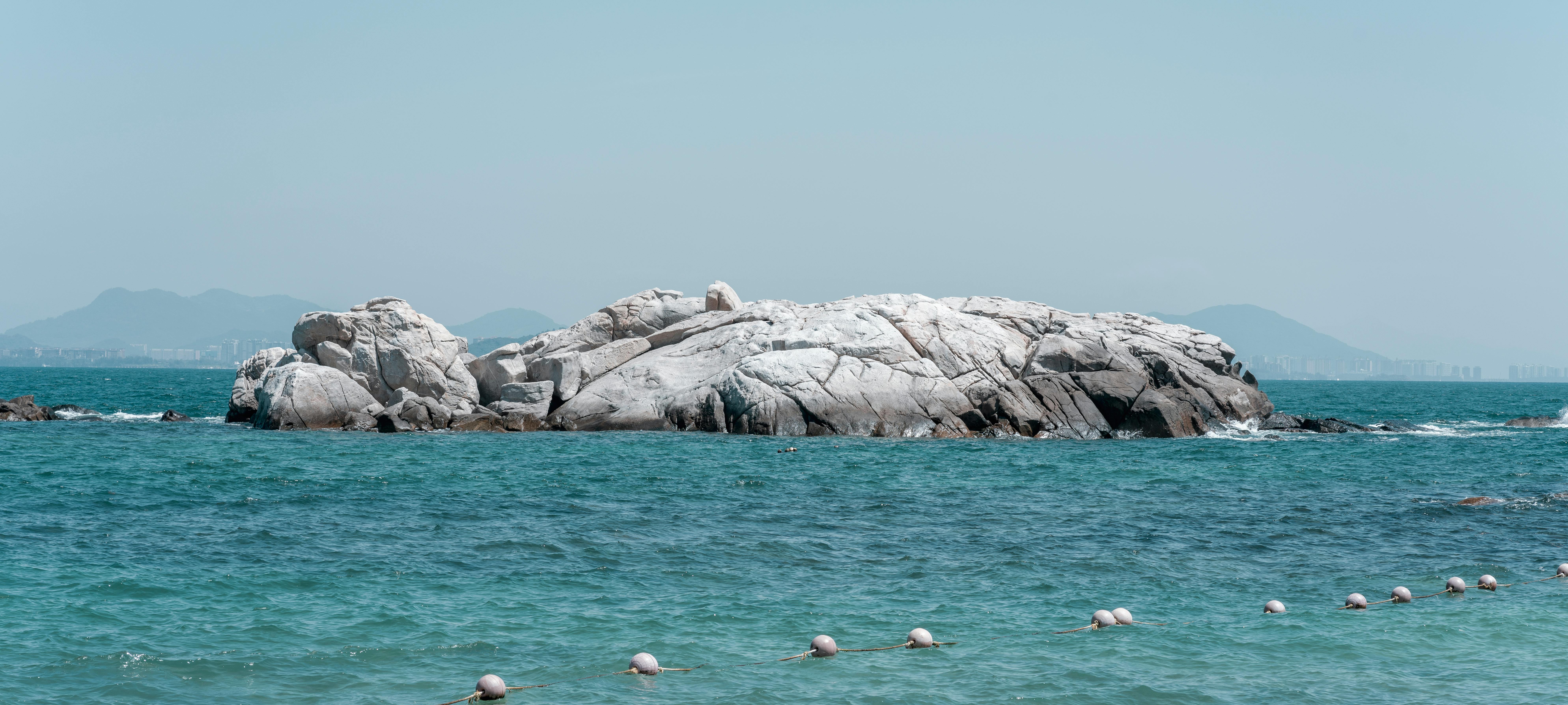 Tranquil scene of a rocky island surrounded by clear blue ocean water with distant mountains.