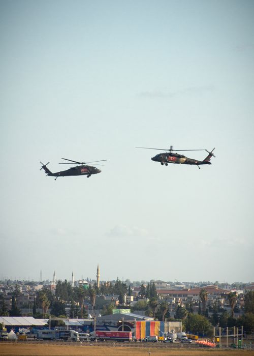 Free Two military helicopters hover above a city, offering a striking scene against the open sky. Stock Photo