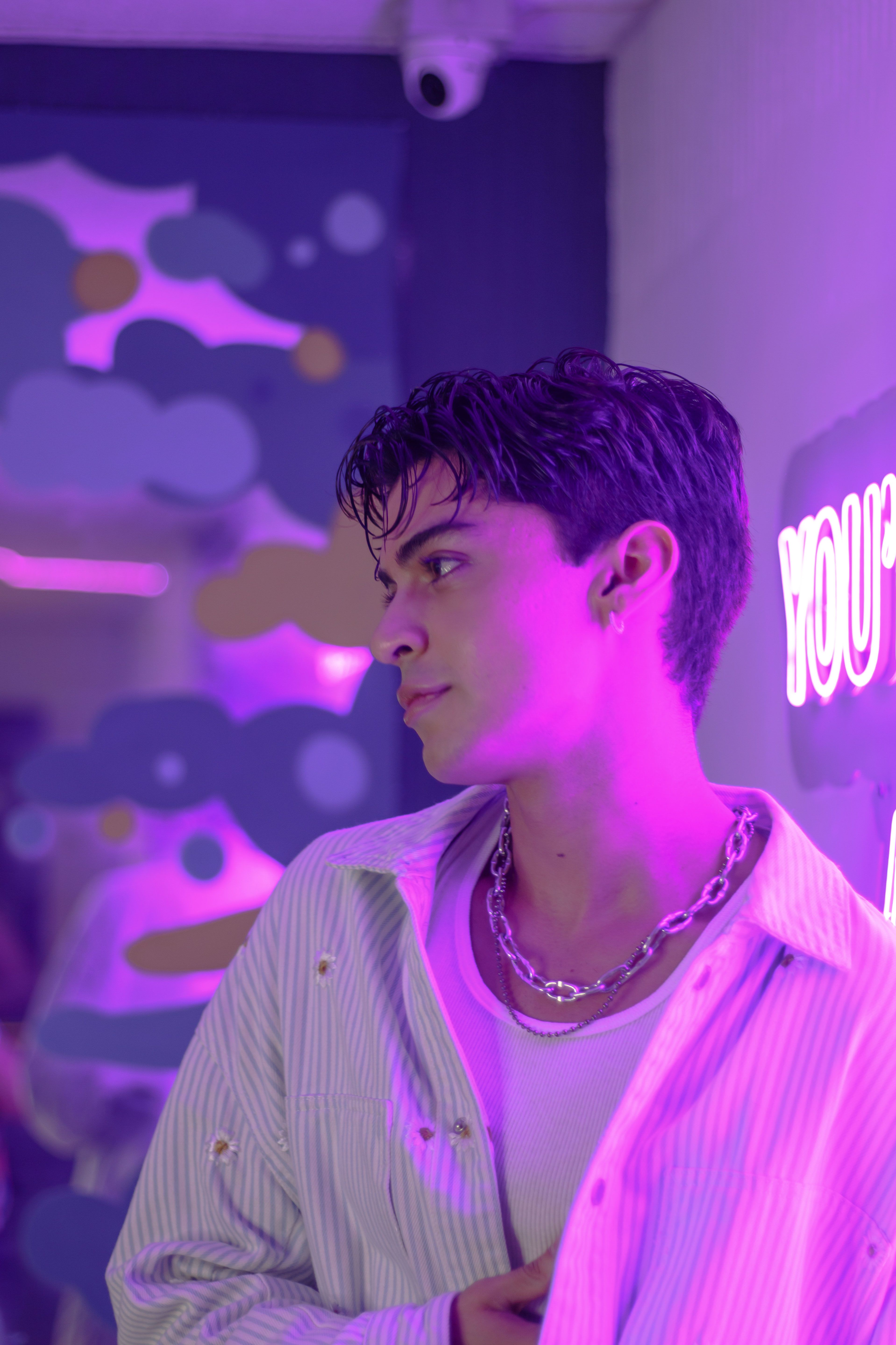 Fotomural Un joven está de pie en una habitación iluminada por neón con un brillo púrpura vibrante en Ciudad de México.