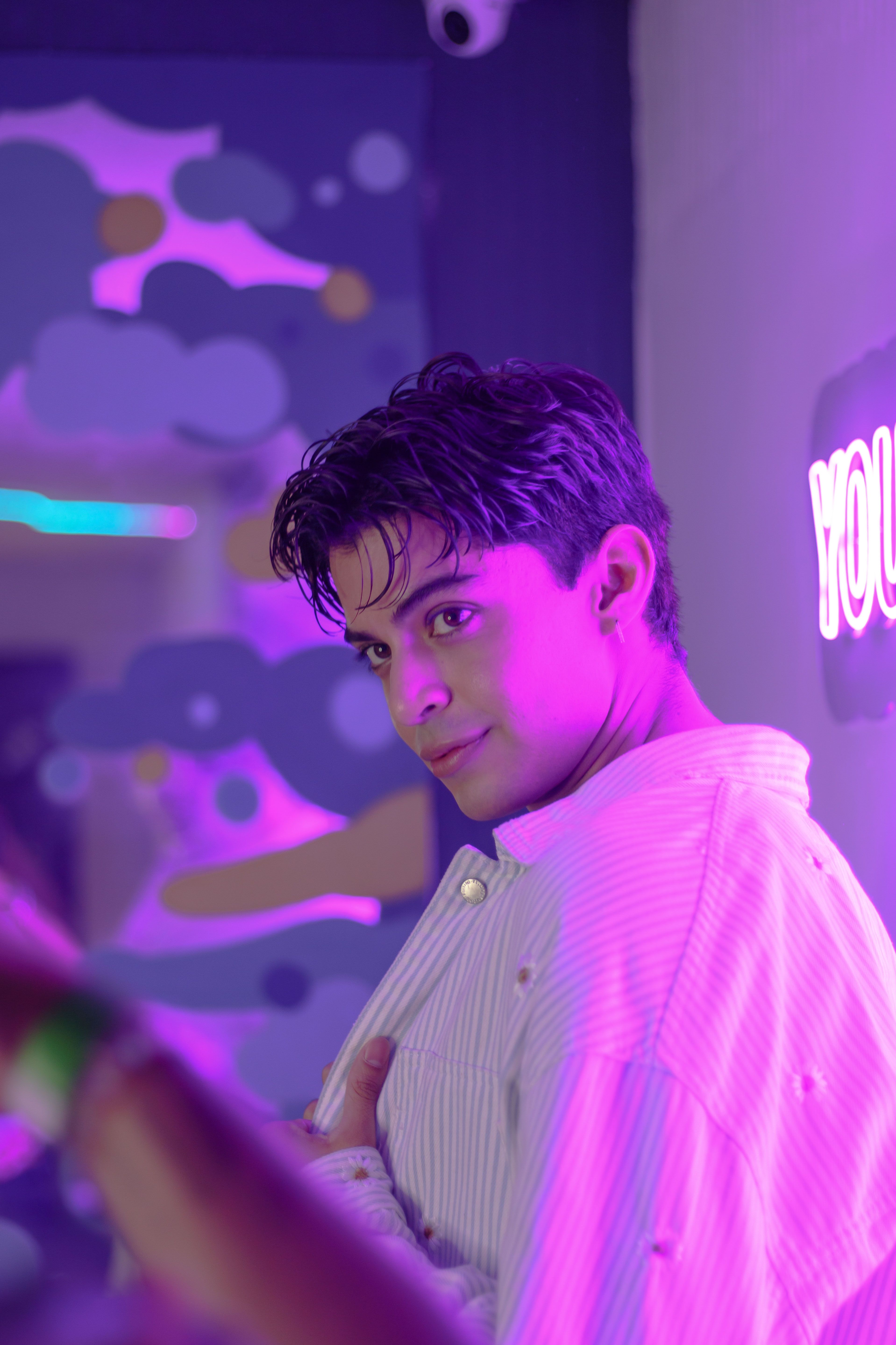 A stylish young man poses indoors with vibrant neon purple lighting in CDMX.
