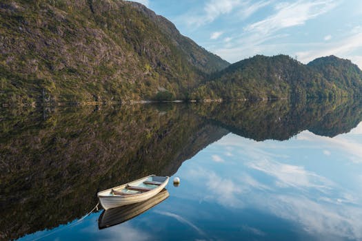 Tranquil scene of a lone boat on a mirrored lake surrounded by lush hills and a clear blue sky, captured in Norway.