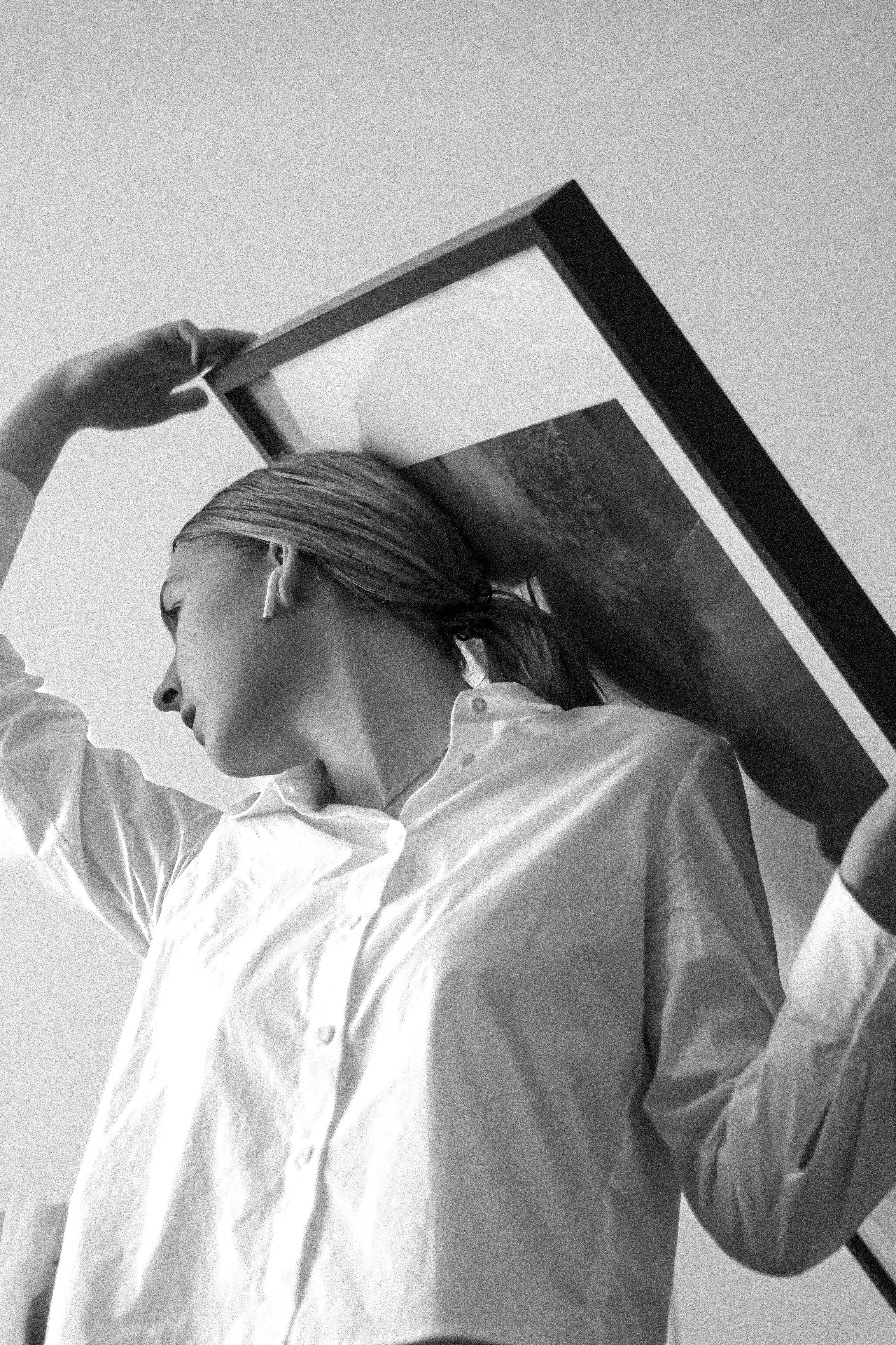 Black and white image of woman holding a frame close to her head.