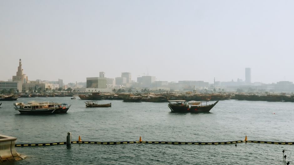 Traditional Dhow boats sailing on the Doha Corniche at sunset in Qatar.