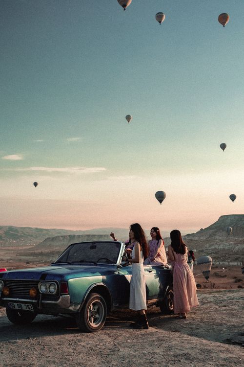 Free Hot air balloons fill the sky over Cappadocia, Turkey, with people enjoying the view from a vintage car. Stock Photo