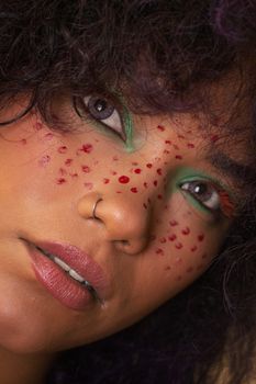Close-up of a woman's face with creative red face paint and green eyeshadow, highlighting artistic expression.