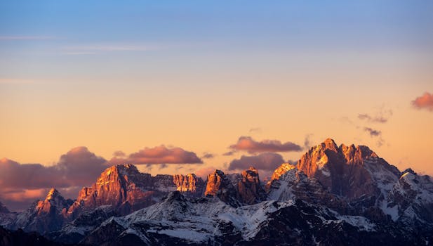 Stunning sunset over the Dolomites mountains with vibrant orange and peach hues.
