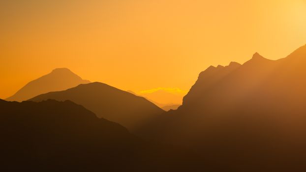 Silhouetted mountains at sunrise with warm orange hues in the Écrins National Park.