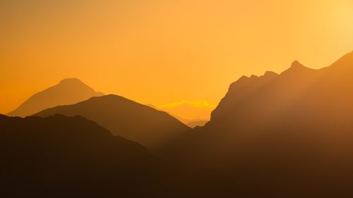 Free Silhouetted mountains at sunrise with warm orange hues in the Écrins National Park. Stock Photo