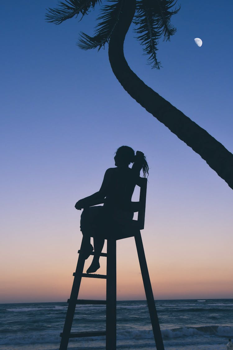 Silhouette Of Woman Sitting On Chair Near Body Of Water