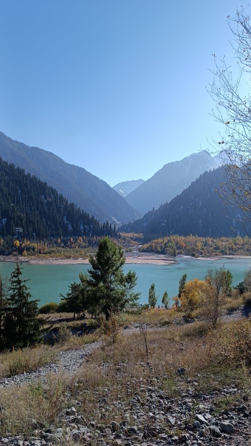 Free A serene mountain lake surrounded by autumn trees and hills under a clear blue sky. Stock Photo