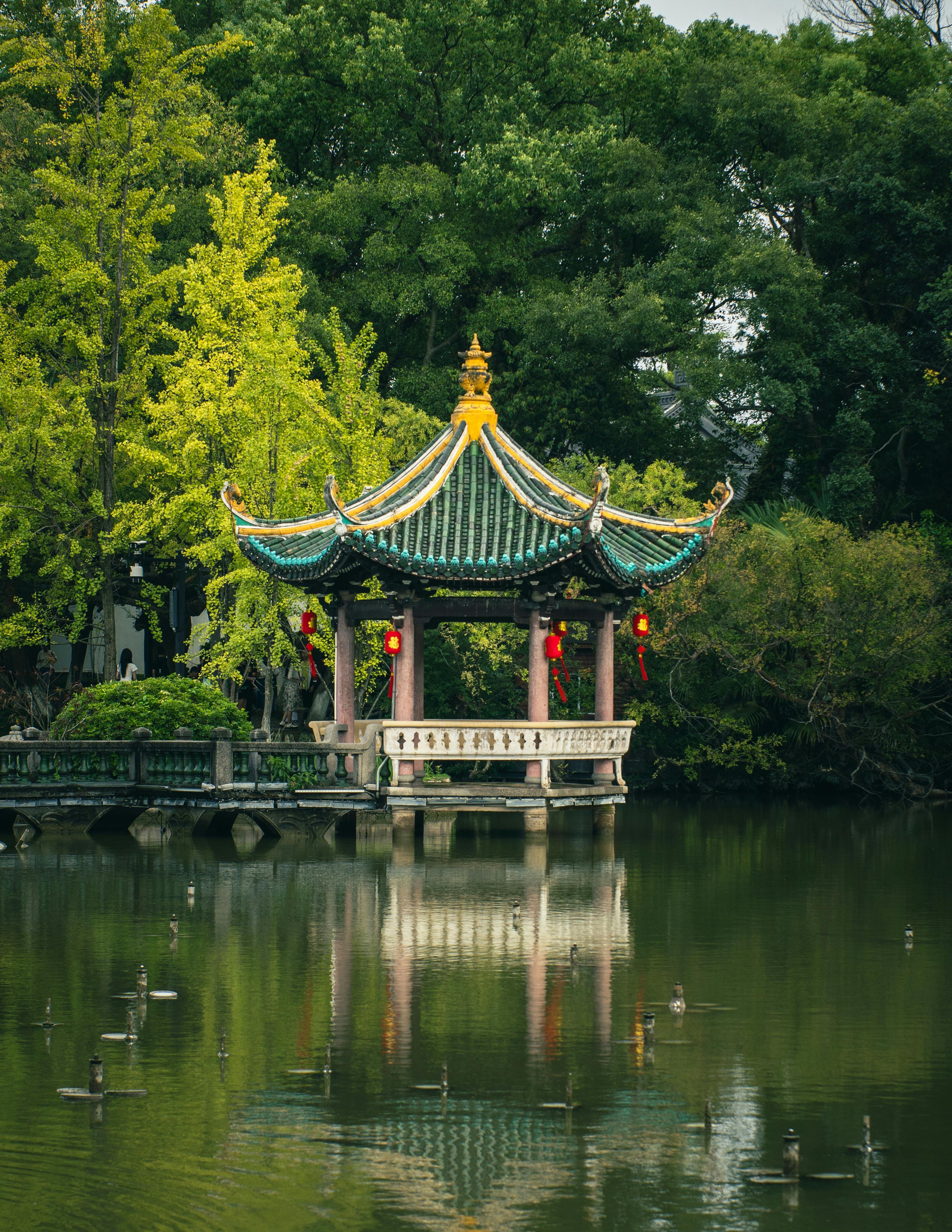 Traditional Chinese pavilion surrounded by lush greenery, reflected on a tranquil lake.