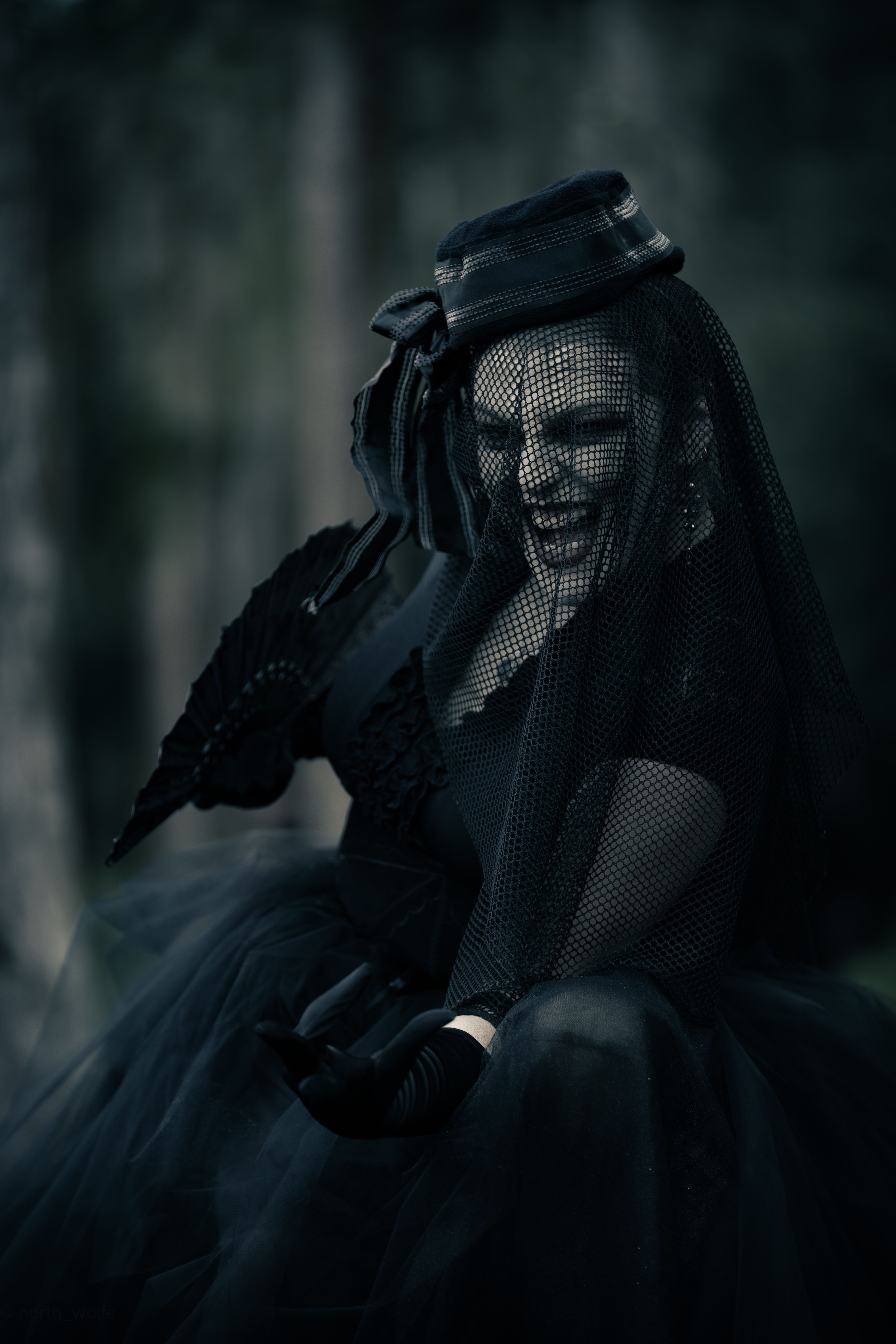 Gothic woman in dark attire with a netted veil and lace umbrella, exuding mystery.