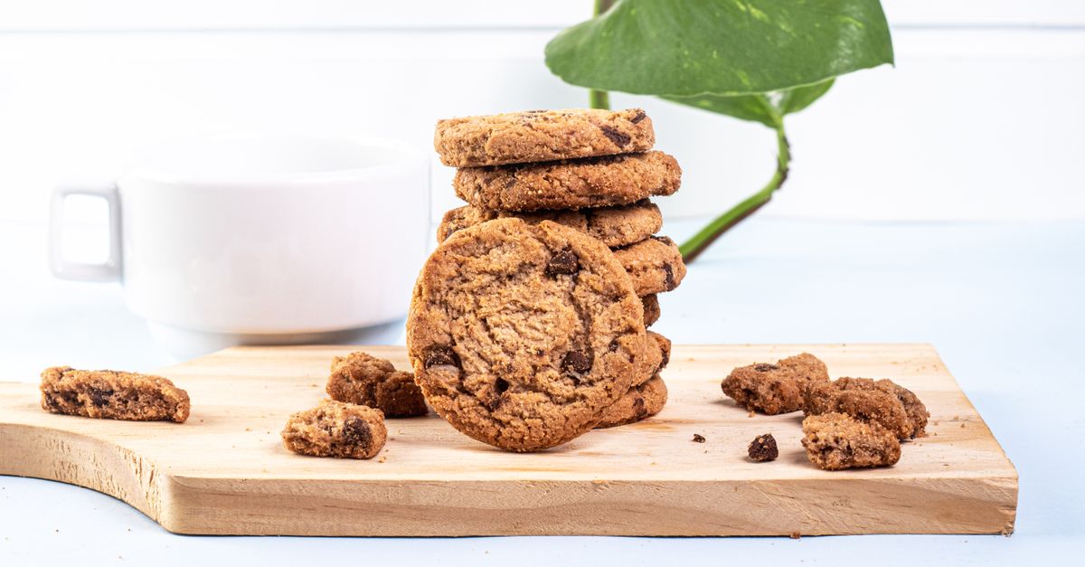 Close-up de cookies de chocolate em uma tábua de madeira com uma xícara ao fundo.