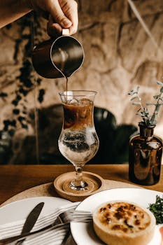 在舒适的咖啡馆里，用手将冰咖啡倒入桌上放有馅饼和餐具的杯子中