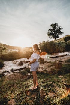 一名妇女站在河边，欣赏着户外自然中的日落美景