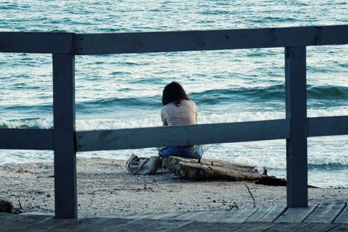 Free A woman sitting alone by the sea, reflecting on life's moments. Captured from behind with ocean waves. Stock Photo