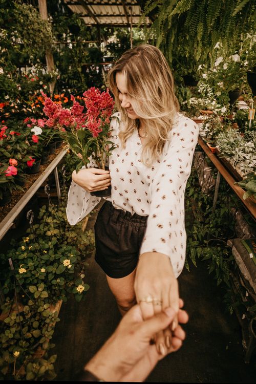Free Woman in a floral greenhouse holding pink flowers, captured in a candid moment. Stock Photo