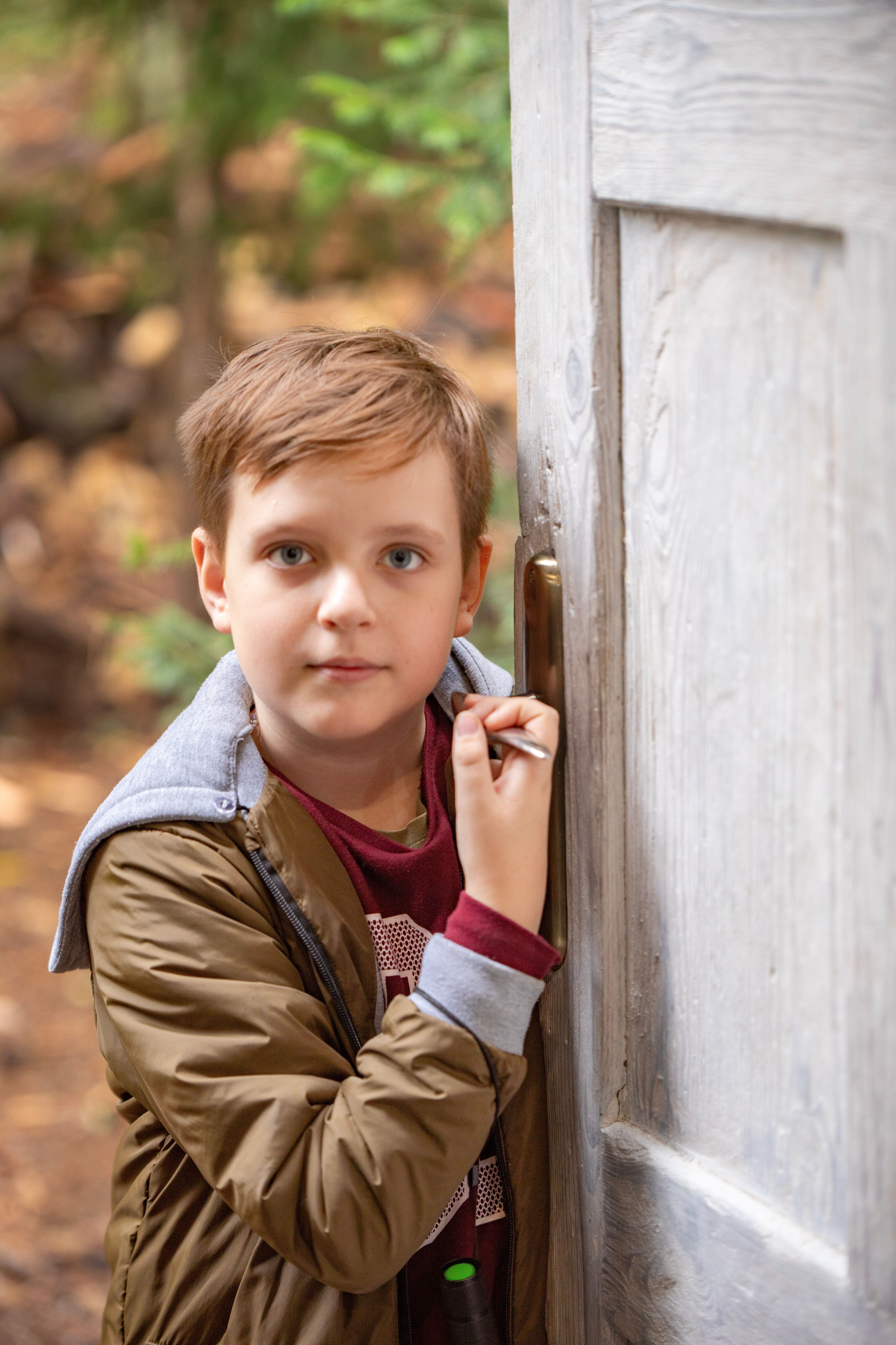 A young boy holding a door handle in a forest. Autumn scene.