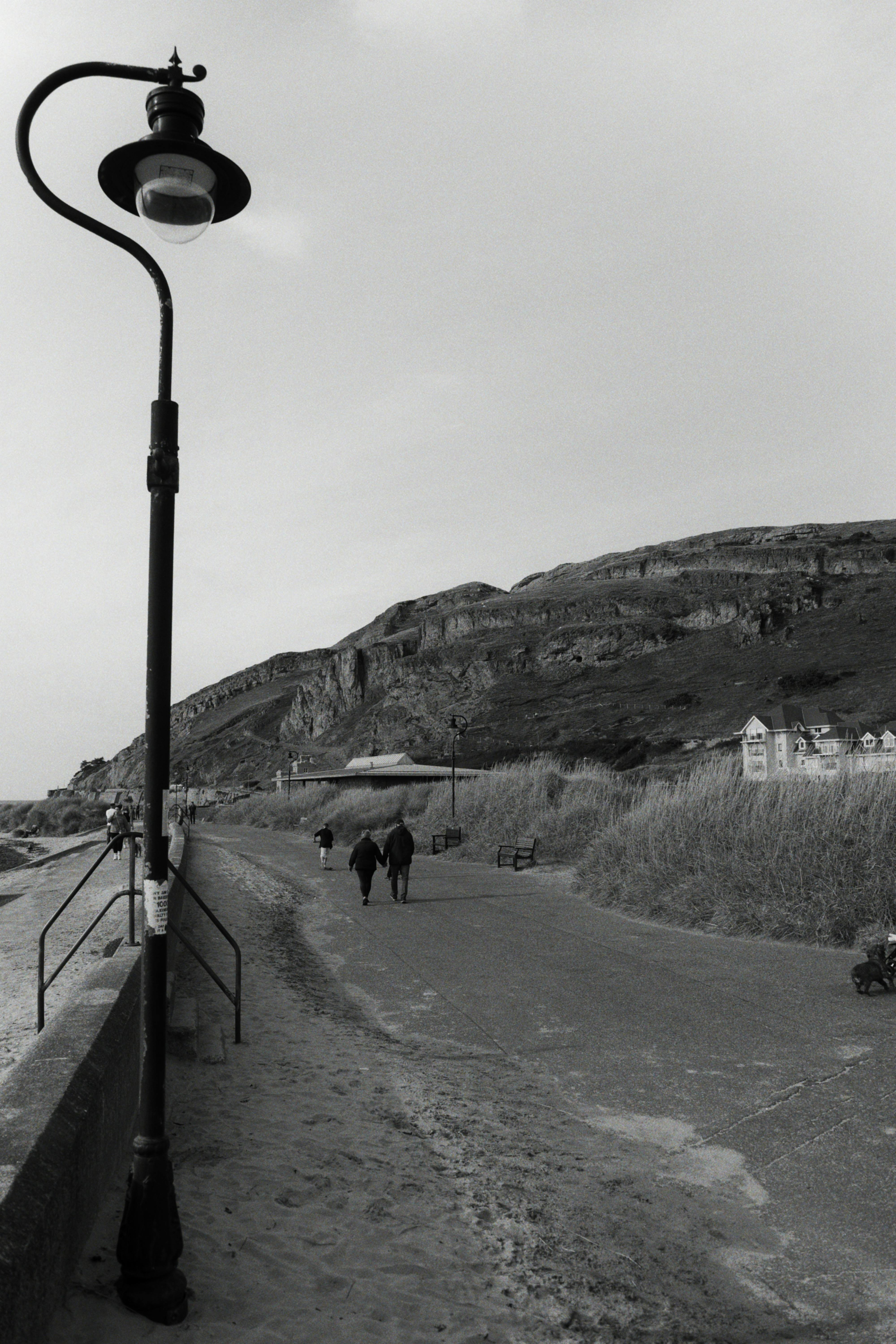 Black and white image of a coastal pathway with streetlamp and cliffs.
