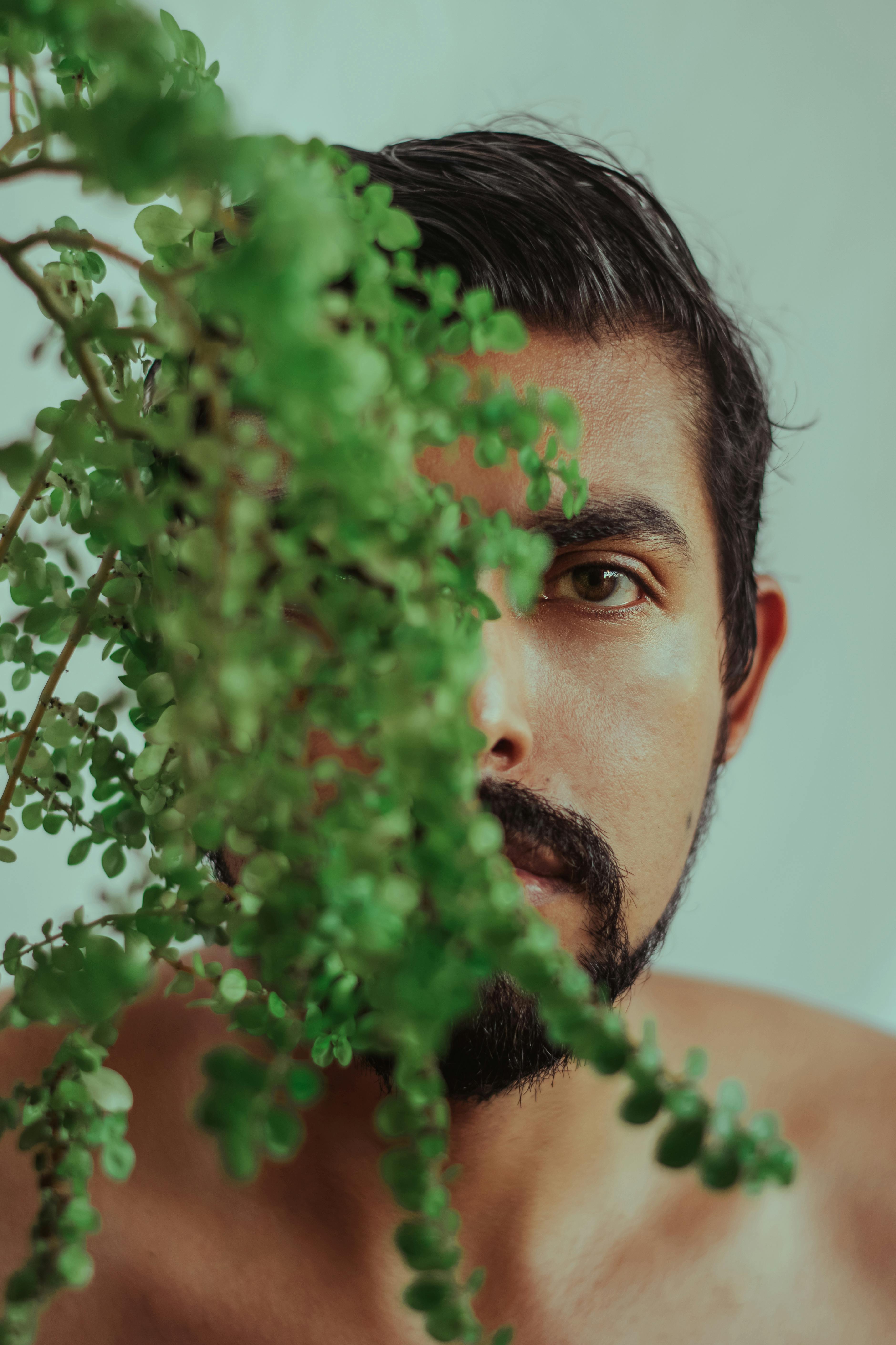 Captivating portrait of a man partially obscured by vibrant green foliage, creating a mysterious and artistic effect.