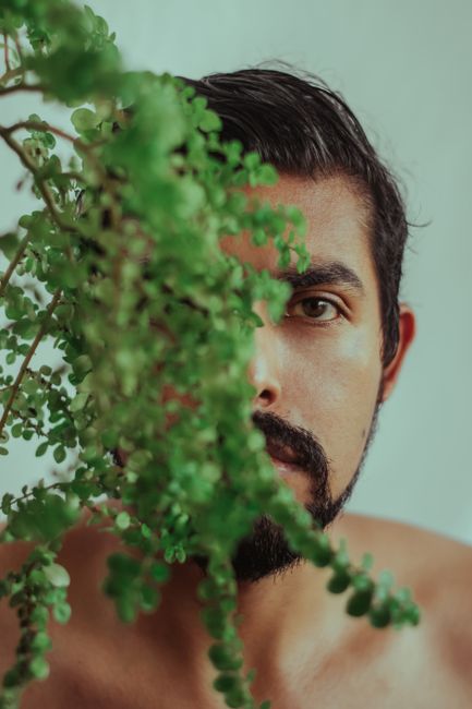 Captivating portrait of a man partially obscured by vibrant green foliage, creating a mysterious and artistic effect.