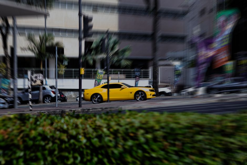 A dynamic shot of a yellow sports car speeding through a bustling city environment in Belo Horizonte.