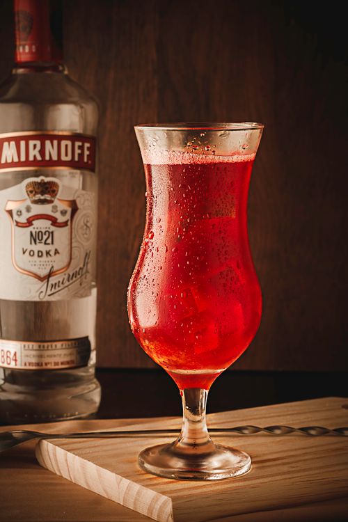 Free Chilled red cocktail in a glass with a vodka bottle backdrop, perfect for party themes. Stock Photo
