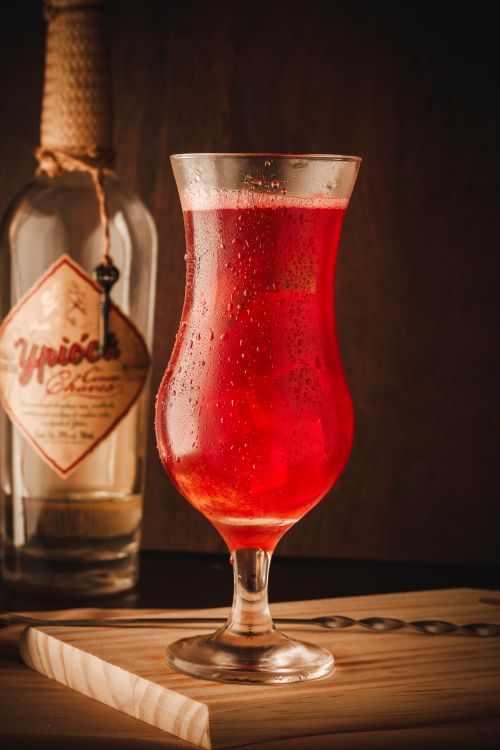 Free Close-up of a vibrant red cocktail glass with a beverage bottle in the background, perfect for lifestyle and food themes. Stock Photo
