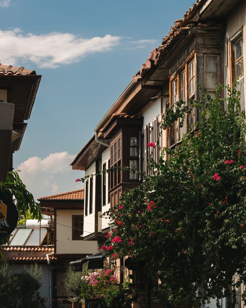 Free Explore a quaint old town street lined with rustic buildings and vibrant flowers under a clear blue sky. Stock Photo