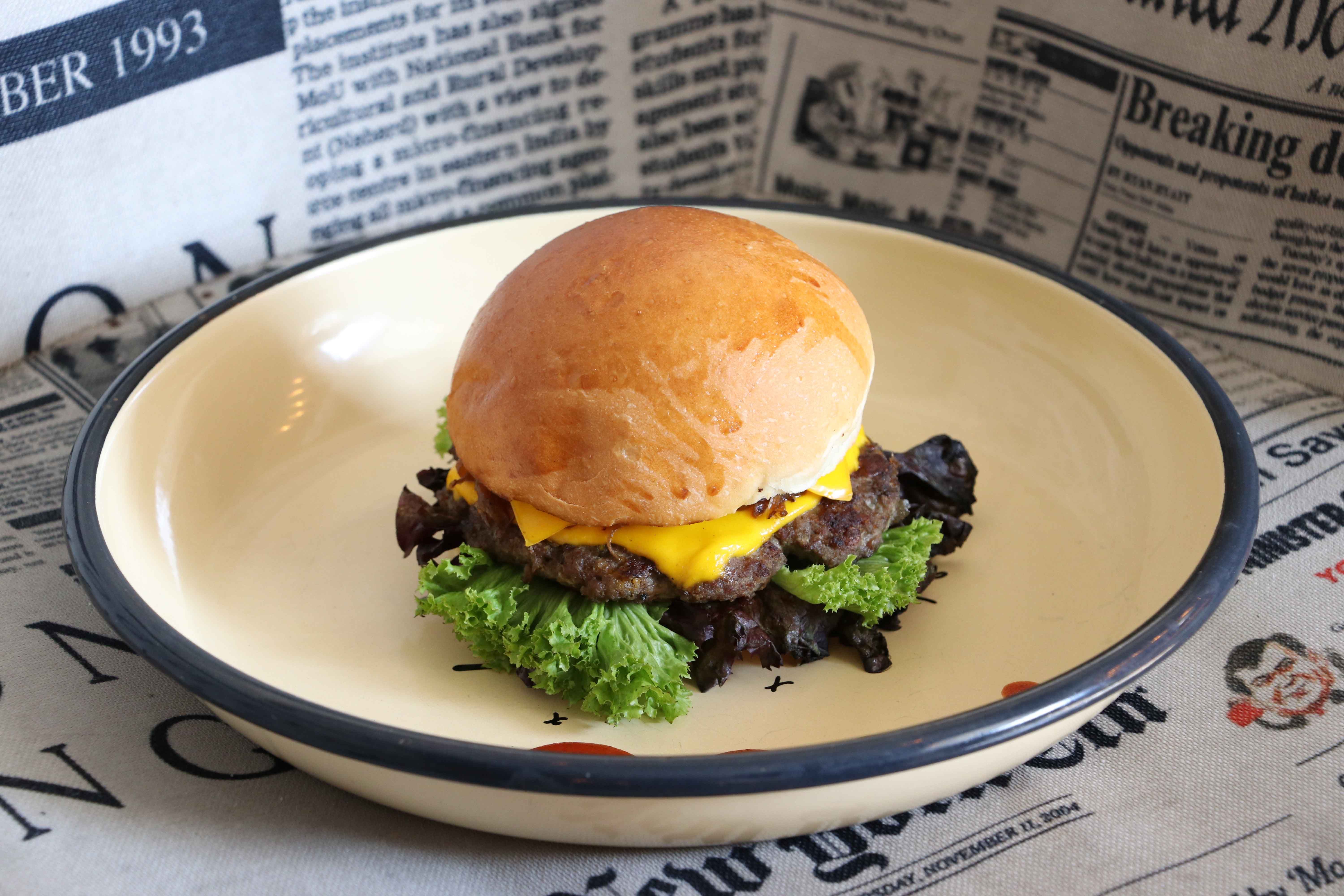 Tasty cheeseburger with lettuce on a plate, surrounded by vintage newspapers.