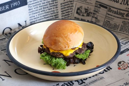 Tasty cheeseburger with lettuce on a plate, surrounded by vintage newspapers.