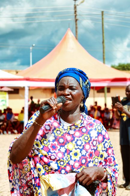A joyful African woman in vibrant attire singing outdoors at a cultural event in Ghana.