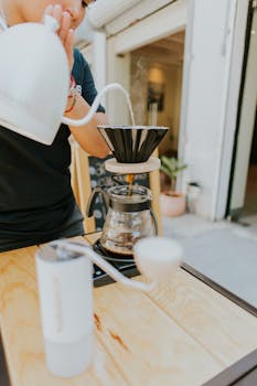 Barista using pour over coffee method in an outdoor cafe setting, emphasizing craft coffee making.