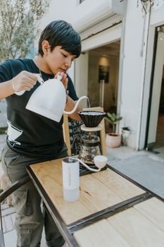 Barista brewing coffee using pour-over technique outside a cozy cafe.