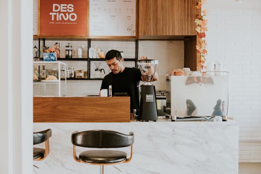 A barista in a contemporary café makes coffee behind a marble counter.