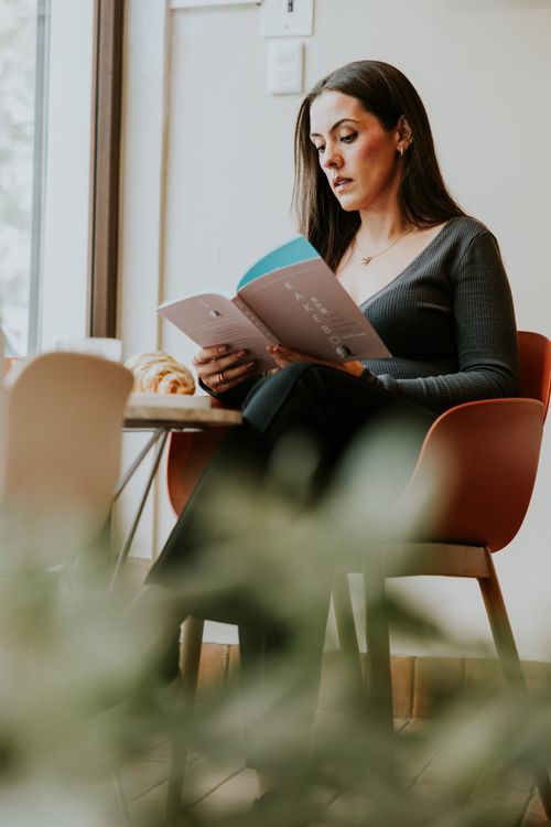 Free Woman enjoying a book and coffee in a modern cafe with a warm ambiance. Stock Photo