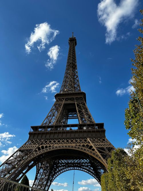 Free The iconic Eiffel Tower on a sunny day with a clear blue sky and scattered clouds. Stock Photo