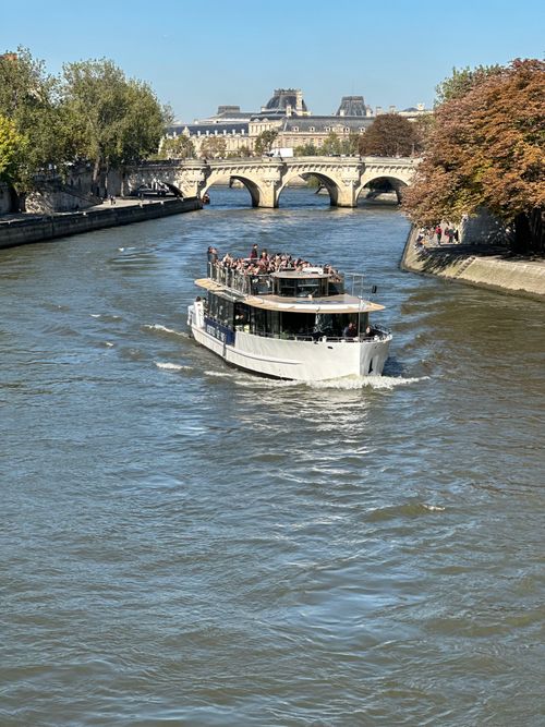Free Tour boat on the Seine River with historic bridge and lush trees on a clear day. Stock Photo