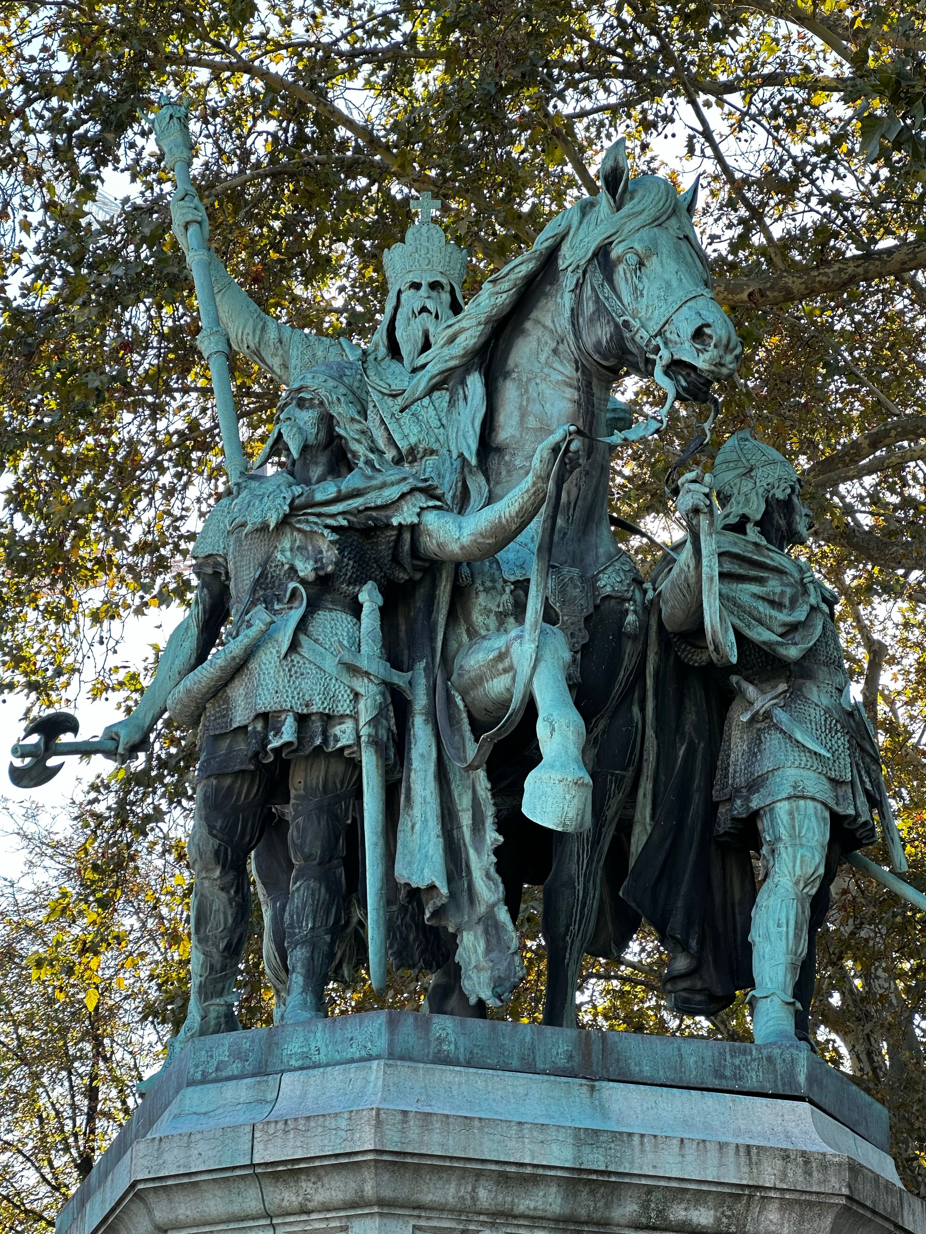 Bronze statue depicting historical figures and horse among trees.
