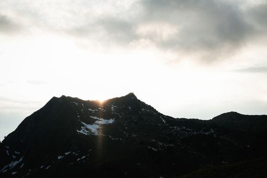 A breathtaking view of sunrise illuminating a snow-capped mountain peak under cloudy skies.