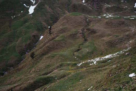 Breathtaking view of a lush green mountain with traces of snow, showcasing natural beauty.