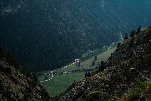 Free A serene mountain valley landscape with a distant cabin nestled among lush greenery. Stock Photo