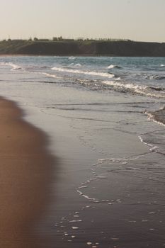 Serene beach scene with soft waves and subdued light at sunrise.