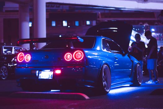 A blue sports car with neon lights parked at night in an urban setting.