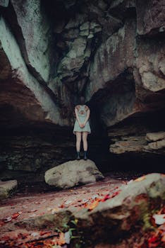 A young woman stands in a dramatic rocky cave, creating an enigmatic atmosphere.