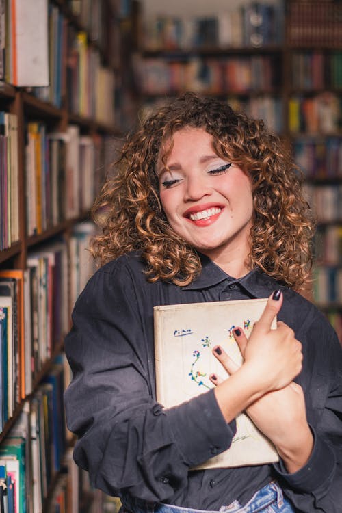 Free Smiling Woman Holding a book  in Library Stock Photo