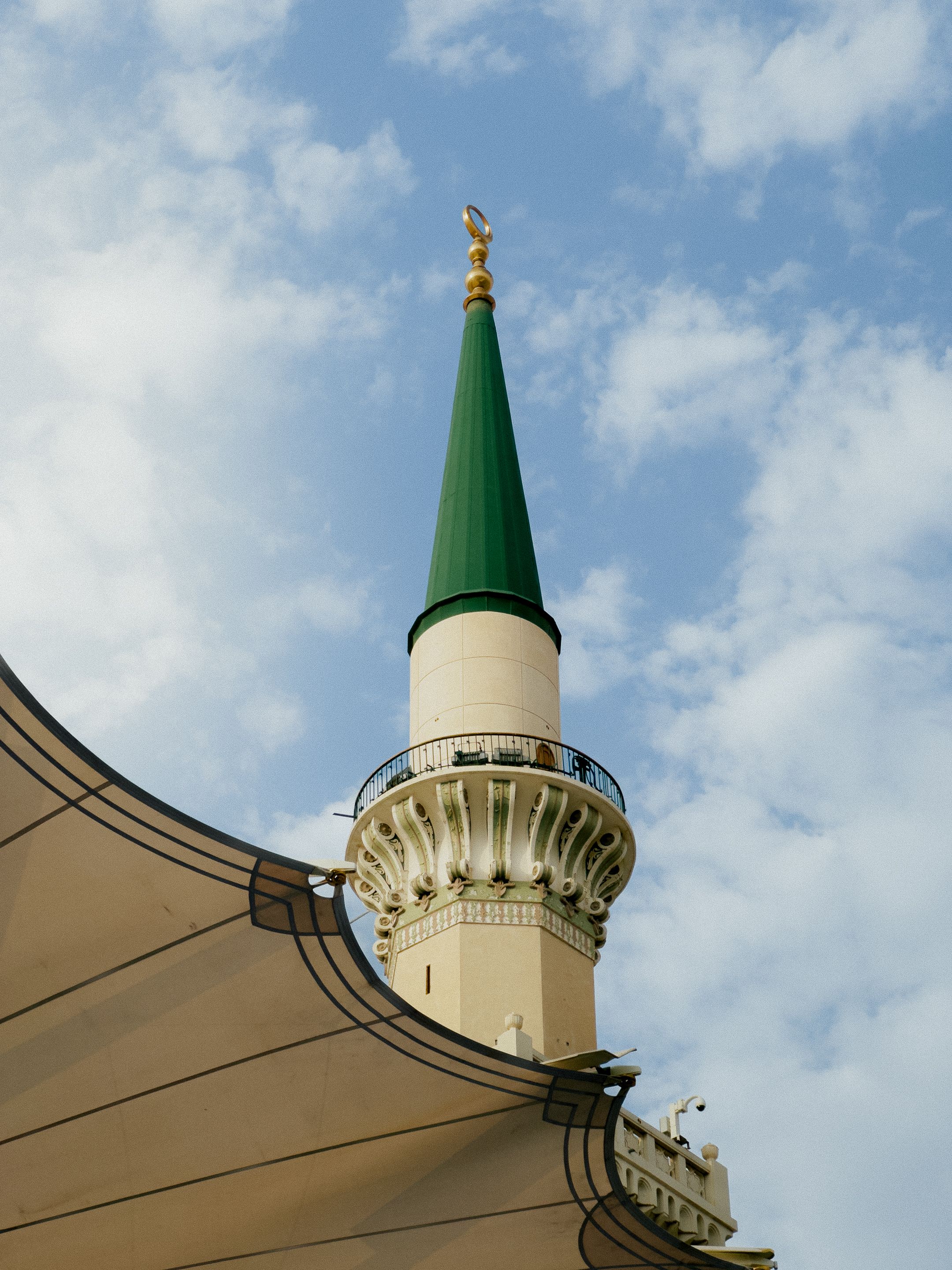 Beautiful view of the minaret and canopy of Al-Masjid An-Nabawi in Medina against a blue sky.