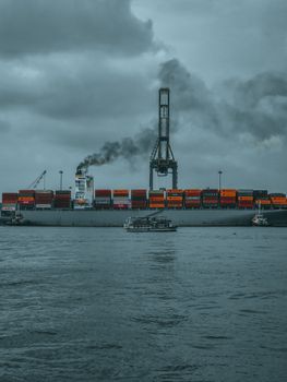A cargo ship emitting smoke in Kochi harbor under moody skies, showcasing industrial maritime transport.
