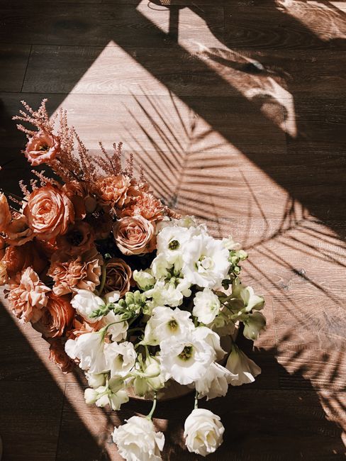 A beautiful bouquet of orange and white flowers casts a shadow on the wooden floor, capturing elegance and romance.