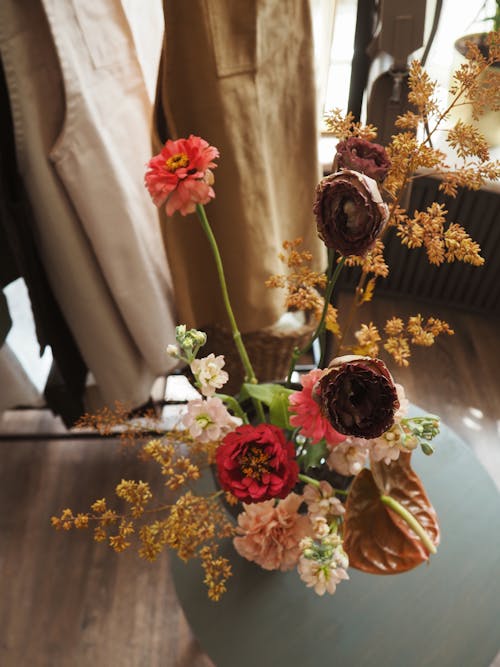 Top view of colorful bouquet of long flowers in vase on coffee table next to clothes on hanger